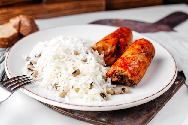 Vista frontal, arroz cozido, juntamente com carne e feijão dentro de chapa branca na mesa de madeira marrom e superfície
