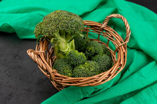 Vista frontal brócolis verde fresco maduro dentro da cesta no tecido verde e piso cinza