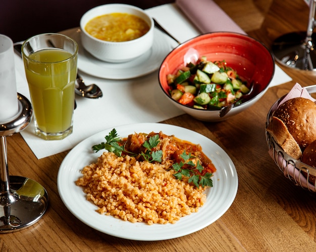 Vista frontal bulgur com carne e molho com sopa de legumes salada e suco em cima da mesa