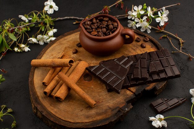 vista frontal canela fresca, juntamente com chocolate amargo na mesa de madeira em torno de flores brancas no chão escuro