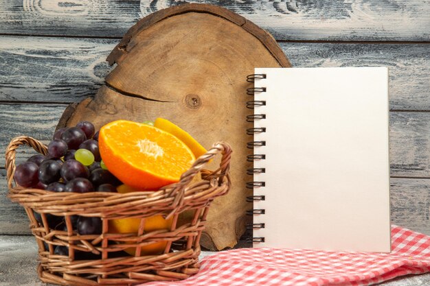 Vista frontal com uvas de frutas frescas e laranjas fatiadas dentro de uma cesta em fundo cinza frutas maduras vitaminas frescas