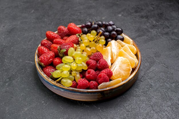 Vista frontal composição de frutas morangos uvas framboesas e tangerinas dentro da bandeja no espaço escuro