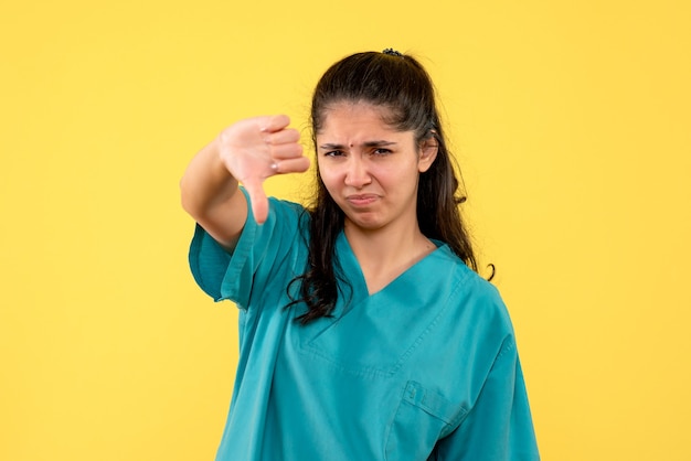 Vista frontal confusa muito médica fazendo sinal de polegar para baixo em fundo amarelo