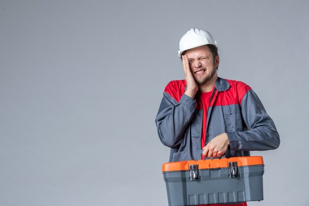 vista frontal, construtor masculino em uniforme segurando a maleta de ferramentas em fundo cinza