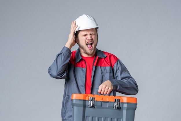 vista frontal, construtor masculino em uniforme segurando a maleta de ferramentas em fundo cinza