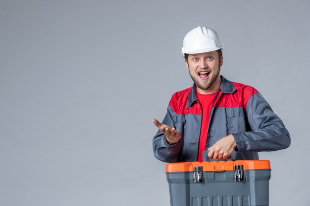 Vista frontal, construtor masculino uniformizado segurando a maleta de ferramentas animado com um fundo cinza