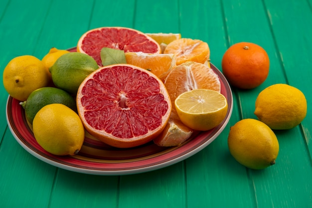 Vista frontal cortada ao meio toranja com laranjas descascadas e limão com limão em um prato sobre fundo verde