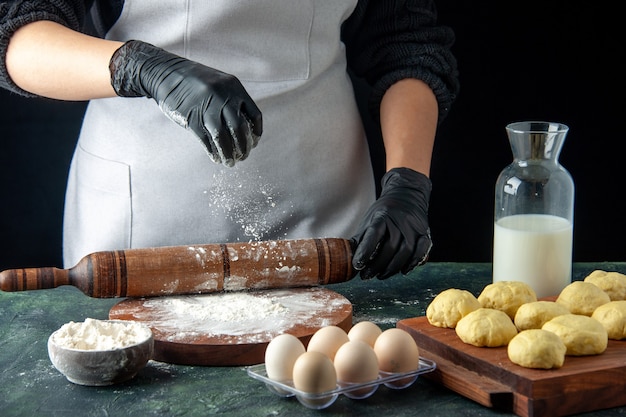 Vista frontal cozinheira desenrolando massa com farinha no escuro cozinha hotcake massa crua assar bolo torta de trabalhador