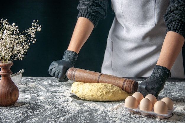 Vista frontal cozinheira desenrolando massa com rolo na massa escura ovo trabalho padaria bolo quente cozinha cozinha