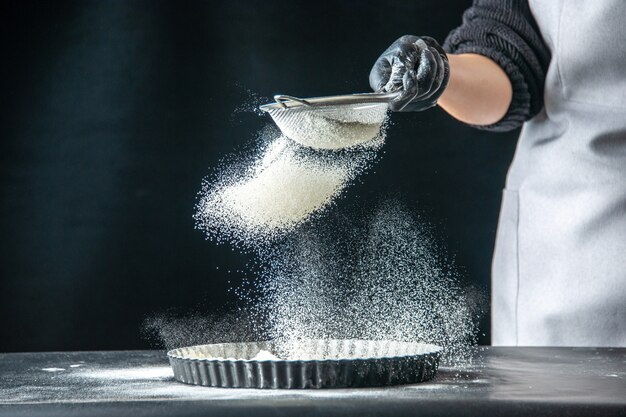 Vista frontal cozinheira despejando farinha branca na frigideira em um ovo escuro padaria hotcake pastelaria cozinha massa