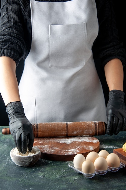 Vista frontal cozinheira esticando a massa com farinha no escuro cozinha hotcake massa crua assar bolo trabalhador torta