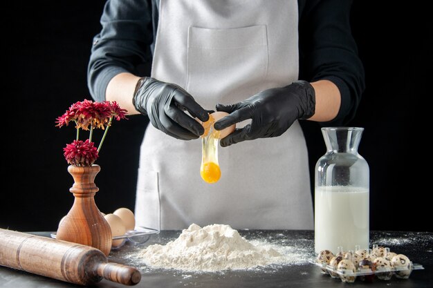 Vista frontal cozinheira quebrando ovos em farinha em um trabalho escuro pastelaria torta padaria cozinhar assar bolo massa de biscoito