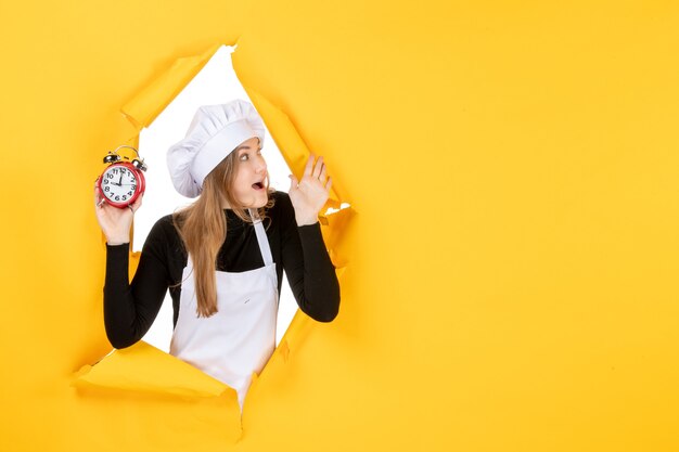 Vista frontal cozinheira segurando relógios em amarelo tempo comida foto cor trabalho cozinha emoção sol cozinha