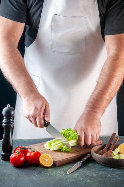 Vista frontal cozinheiro masculino cortando aipo na parede escura dieta refeição foto alimentos saudáveis cores