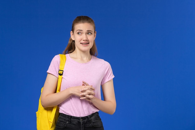 Foto grátis vista frontal da aluna em uma camiseta rosa com mochila amarela, parada na parede azul