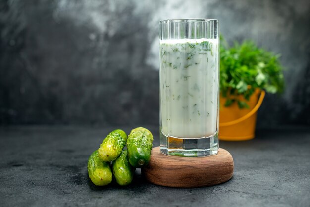Vista frontal da bebida de iogurte atlama com verduras na tábua de madeira pepinos em vasos de plantas na mesa isolada cinza local de cópia