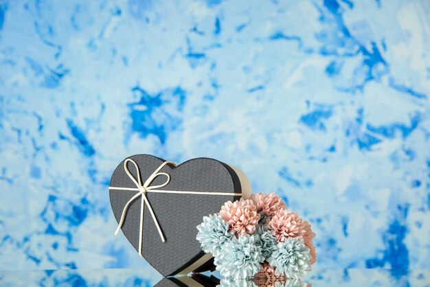Vista frontal da caixa de presente de coração com flores coloridas de capa preta em fundo azul desfocado