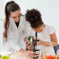 Foto grátis vista frontal da cientista fêmea ensinando menina a olhar através do microscópio
