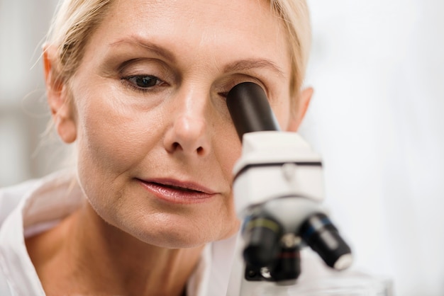 Vista frontal da cientista feminina no laboratório olhando através do microscópio