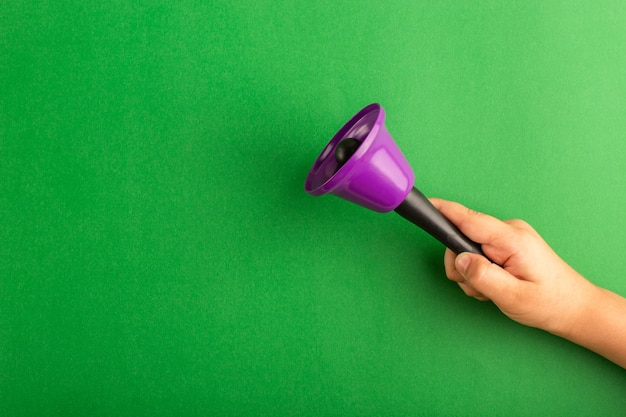 Vista frontal da criança segurando um sino roxo na superfície verde