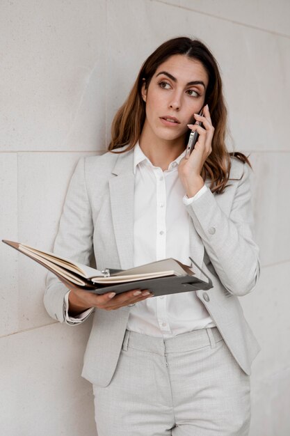 Vista frontal da elegante mulher de negócios com agenda falando ao telefone