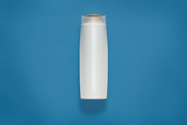 Vista frontal da garrafa de cosméticos de plástico branco em branco isolada no estúdio azul, recipiente cosmético vazio, mock-se e copie o espaço para propaganda ou texto promocional. Conceito de beuity.