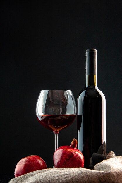 Vista frontal da garrafa de vinho com uma taça de vinho no fundo preto