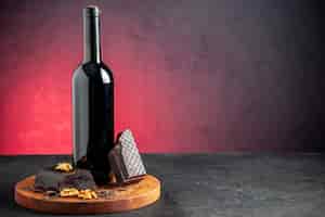Foto grátis vista frontal da garrafa de vinho, pedaços de nozes de chocolate amargo na placa de madeira sobre fundo vermelho
