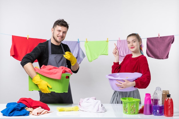 Vista frontal da hora de lavar o homem e a esposa segurando roupas de mesa atrás das roupas de mesa na corda na parede branca