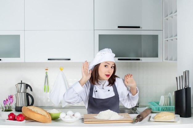 Vista frontal da jovem chef feminina de uniforme ouvindo as últimas fofocas na cozinha branca