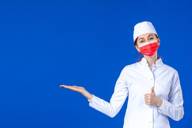 Vista frontal da jovem enfermeira em traje médico com máscara vermelha em azul