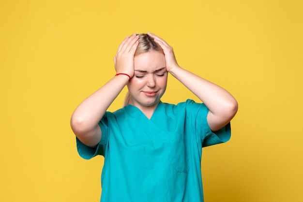 Vista frontal da jovem médica com camisa médica e dor de cabeça na parede amarela