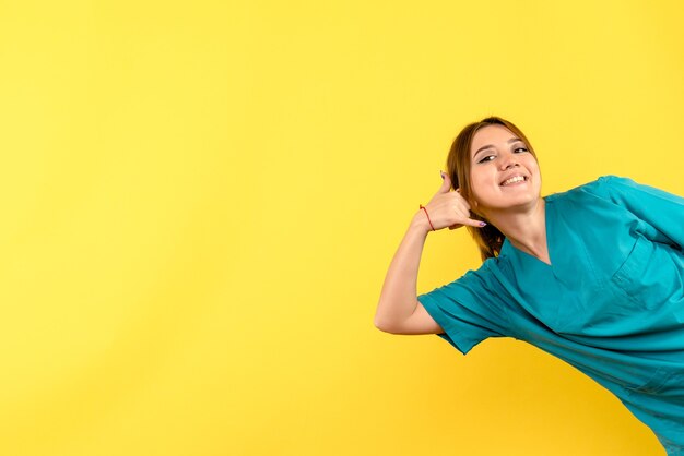 Vista frontal da jovem médica sorrindo na parede amarela