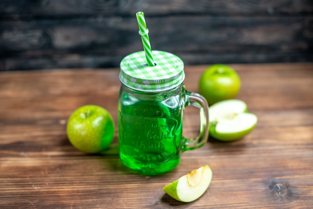 Vista frontal da lata de suco de maçã verde com maçãs frescas em uma mesa de madeira.