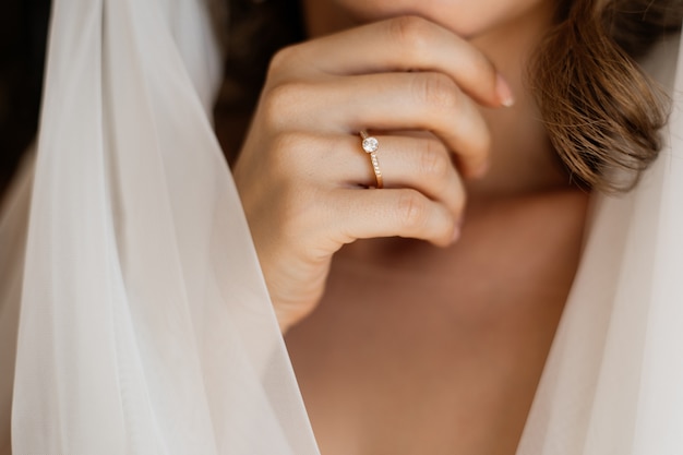 Vista frontal da mão da noiva com um anel de noivado perto do pescoço e véu de noiva