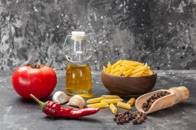 Vista frontal da massa italiana crua com ovos, tomate e óleo no fundo cinza claro