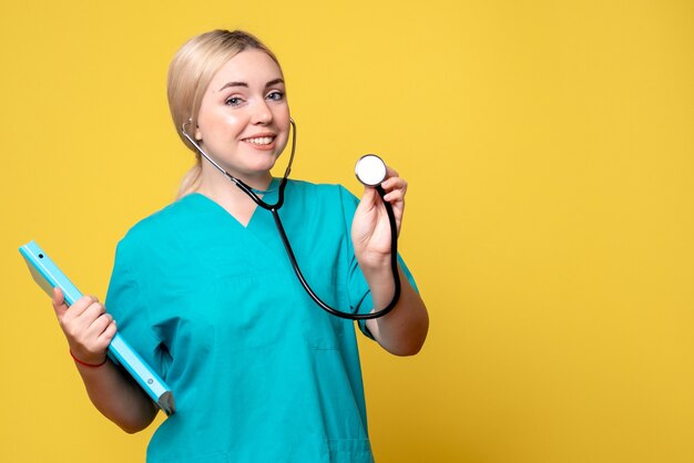 Vista frontal da médica com análise e estetoscópio na parede amarela