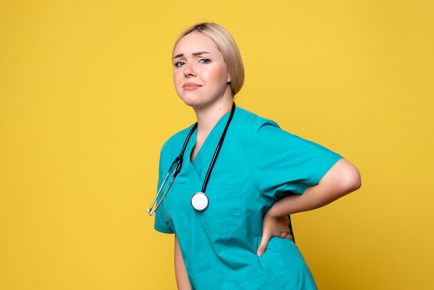 Vista frontal da médica com camisa médica e estetoscópio na parede amarela