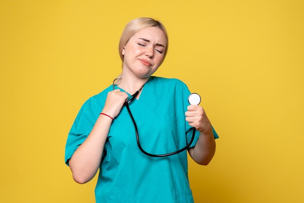 Vista frontal da médica com camisa médica e estetoscópio na parede amarela