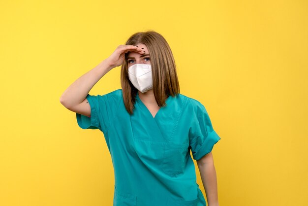 Vista frontal da médica com máscara na parede amarela