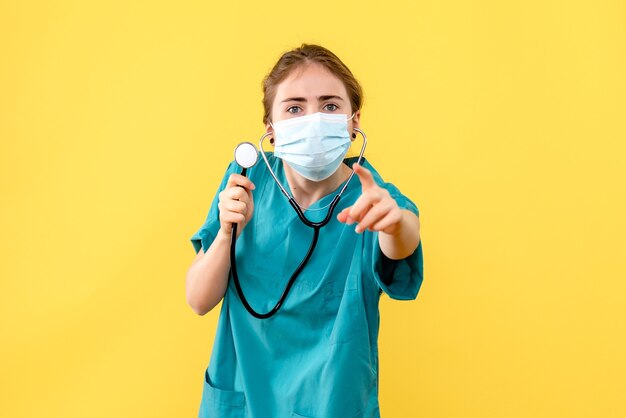 Vista frontal da médica com máscara sobre fundo amarelo-claro vírus da saúde pandêmico covid