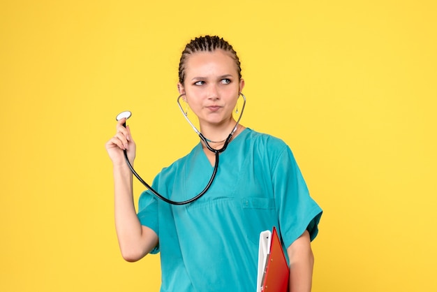 Vista frontal da médica em traje médico com estetoscópio e análise na parede amarela