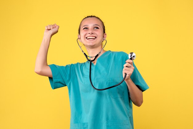 Vista frontal da médica em traje médico com estetoscópio na parede amarela