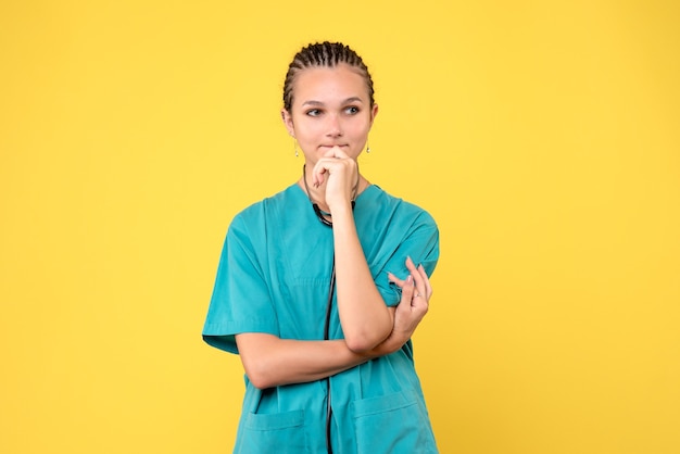 Vista frontal da médica em traje médico na parede amarela