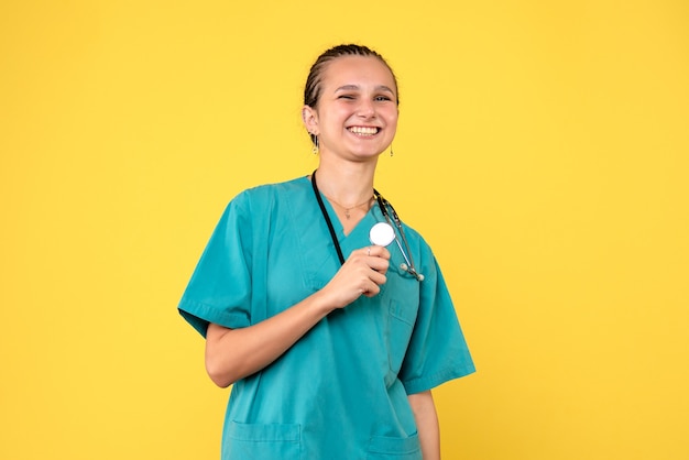 Vista frontal da médica em traje médico na parede amarela