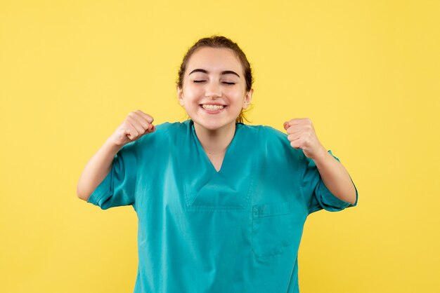 Vista frontal da médica em traje médico regozijando-se na parede amarela