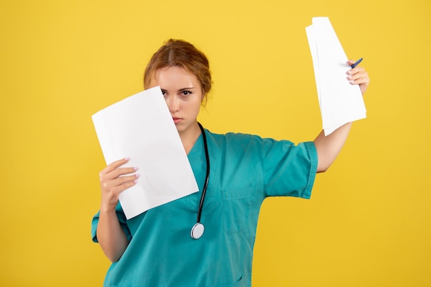 Vista frontal da médica em traje médico segurando análise na parede amarela