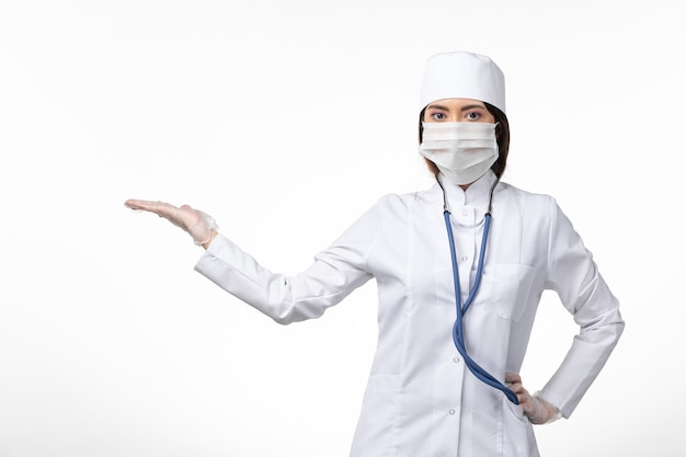 Vista frontal da médica em um terno médico branco com uma máscara devido a uma pandemia no balcão branco.