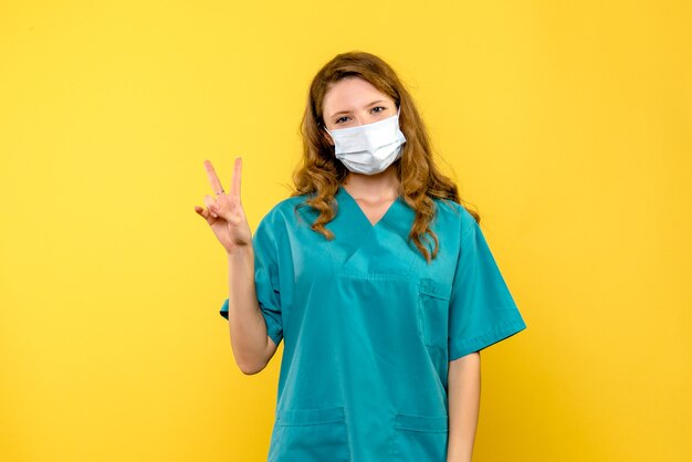 Vista frontal da médica sorrindo com máscara na parede amarela