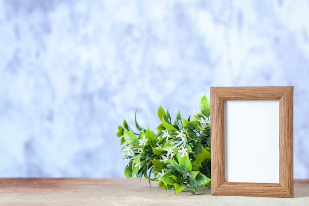 Foto grátis vista frontal da moldura vazia marrom em pé sobre a mesa e a flor na superfície desfocada